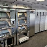 bakkerij machine kopen - Een rij commerciële pizzaovens en metalen bakkerijmachines in een professionele keukensetting. - theovanvliet.nl